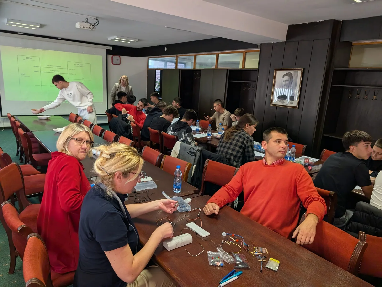 Učesnici radionice za stolovima sa elektronskim komponentama i eksperimentalnim pločama.